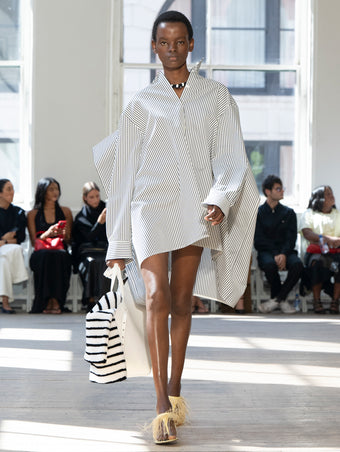 Image of model walking Proenza Schouler SS25 Runway wearing Isla Dress in Stripe Cotton Silk Poplin in  Navy Multi and Days Carryall in Off-White Smooth Calf in OFF-WHITE and Tee Feather Thong Sandal in RESIN