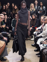 Model Walking In Proenza Schouler Fall Winter 2024 Runway Show Wearing Cruz Sweater In Charcoal Wool Viscose Knit, Avalon Skirt In Black Lacquered Knit, Tube Scarf In Charcoal Wool Viscose Knit, Split Tote In Black Nappa, Silo Bag In Black Na