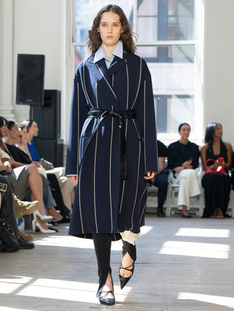 Image of model walking Proenza Schouler SS25 Runway wearing Marina Coat in Stripe Bi-Stretch Viscose in Navy Multi and Hunter Top in Stripe Cotton Silk Shirting in Pale Blue Multi and Zip Legging in Technical Jersey in Black and Slash Slingback Pump in BLACK