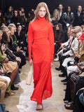 Model walking in Proenza Schouler Fall Winter 2024 Runway show wearing PAULA DRESS IN RED SHEER CREPE JERSEY, STILTSMAN STIRRUP IN BLACK COMPACT JERSEY, Silo Bag in Beige Nappa, and TEE TOE RING SANDAL IN BLACK NAPPA