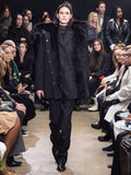 Model Walking in Proenza Schouler Fall Winter 2024 Runway Show Wearing Wilder Coat in Black Technical Nylon, Archer Jacket in Black Wool Twill , Rio Top in Black Tulle Jersey, Teddy Pant in Black Wool Twill, Flip Shoulder Bag in Black Eel, and Chelsea  Bronco Ankle Boots in Black Brushed Calf