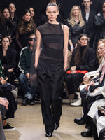 Model Walking in Proenza Schouler Fall Winter 2024 Runway Show Wearing Aurora Top in Black Crepe Chiffon / Wool Gabardine, Teddy Pant in Black Double Weave Viscose Organza, and Tee Ankle Boots in Black Slick Nappa