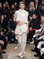 Model Walking in Proenza Schouler Fall Winter 2024 Runway Show Wearing Toni Dress in Ivory Textured Boucle Knit, Blanket in Ivory Textured Boucle Knit, Bond Bag in Cream Embossed Ostrich Calf, Thin Belt in Black Nappa, and Tee Over the Knee Boots in Ecru Viscose Knit