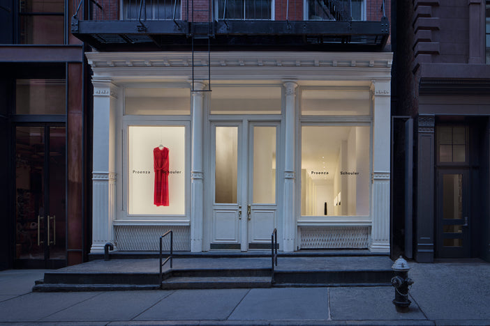 Exterior image of new Proenza Schouler flagship store at 153 Mercer Street. Image of a white building exterior with a red dress hanging in the front window.