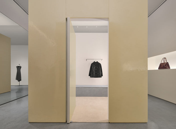 Interior of new Proenza Schouler flagship store at 153 Mercer Street. Image of large resin cube containing a dressing room with a black jacket hanging on a rail.