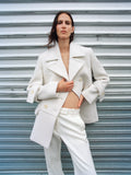 Image of model wearing Rowen Coat in Eco Double Face Wool in ecru, standing against metal wall