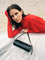 Cropped image of model laying across covered car wearing Paula Dress in Sheer Crepe Jersey in red, carrying Silo Bag in Ostrich Embossed Calf in black