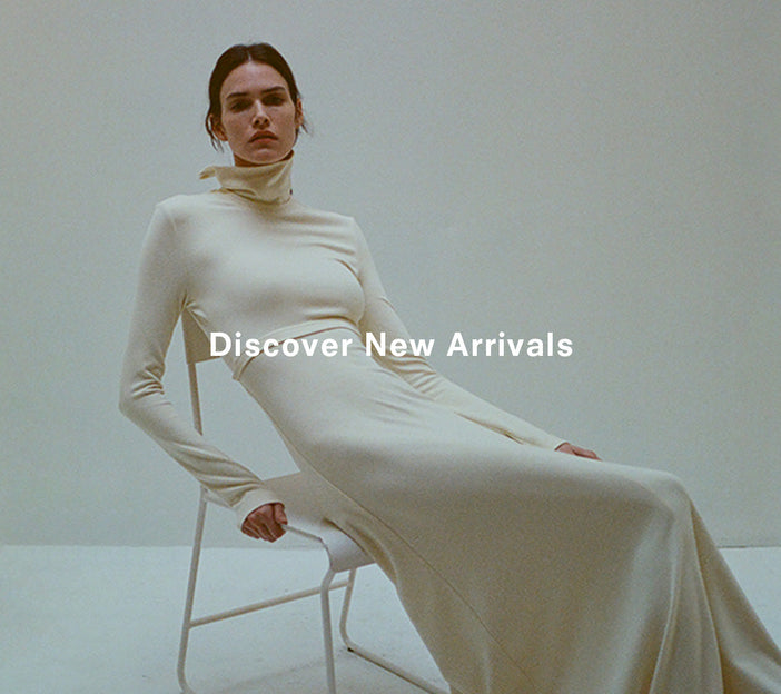 Image of model sitting in white metal chair, wearing Jayne Dress in Brushed Rib in pale yellow, 'Discover New Arrivals' overlaid