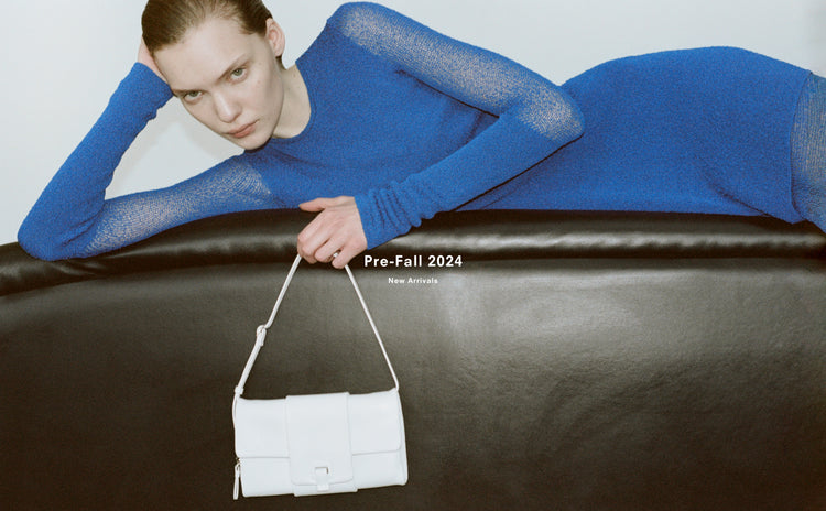 Image of model laying across black leather couch, wearing Anita Dress in Knit Sheer Mesh in bright blue, carrying Flip Shoulder Bag in optic white, 'Pre-Fall 2024, New Arrivals'