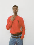 Cropped image of model wearing Harrison Monogram Sweater in Wool Jacquard in red, Ellsworth Jean in medium blue, styled with Square Slider Belt in black and Smyth Pant in Leather in black.