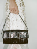 Cropped image of a model's hand holding Flip Shoulder Bag in Eel in black.