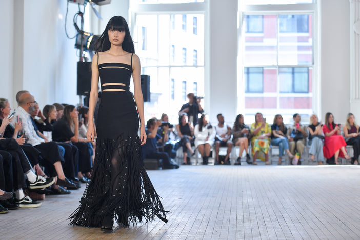 Wide image of model Shuqi Lan walking the SS25 Proenza Schouler fashion show in a black fitted dress with a fringe skirt 