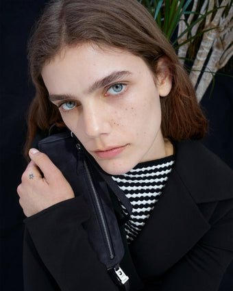 Cropped image of model wearing Prescott Top in Matte Viscose Crepe in black and Marine Jacket in Bi-Stretch Suiting in black, holding Silo Bag in Kid Suede in navy